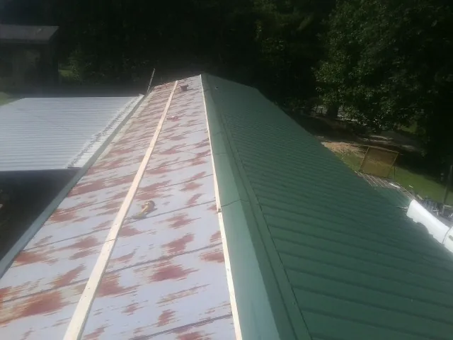 Old rusted panels beside newly installed green metal roofing — Wind Damage Roof Repair by Roofing Brothers in Flat Rock