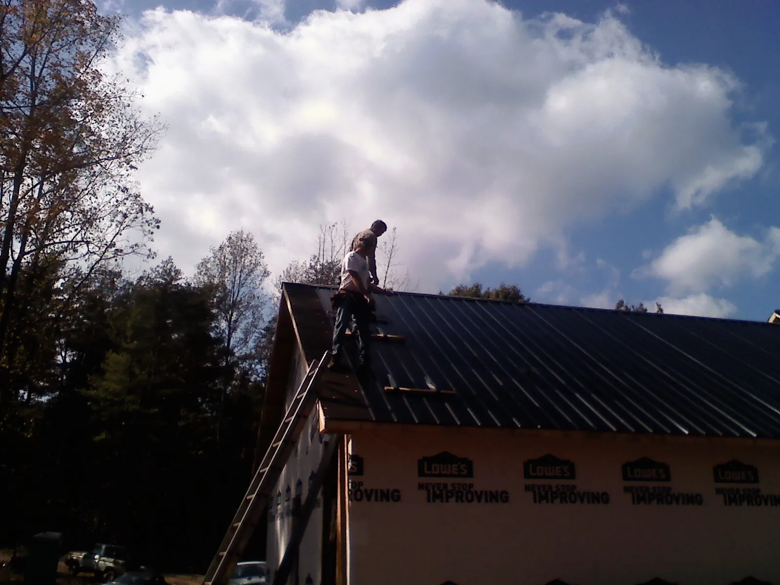 Roofer fastening dark metal panels high against a cloudy sky, from a Roof Inspection job in Flat Rock