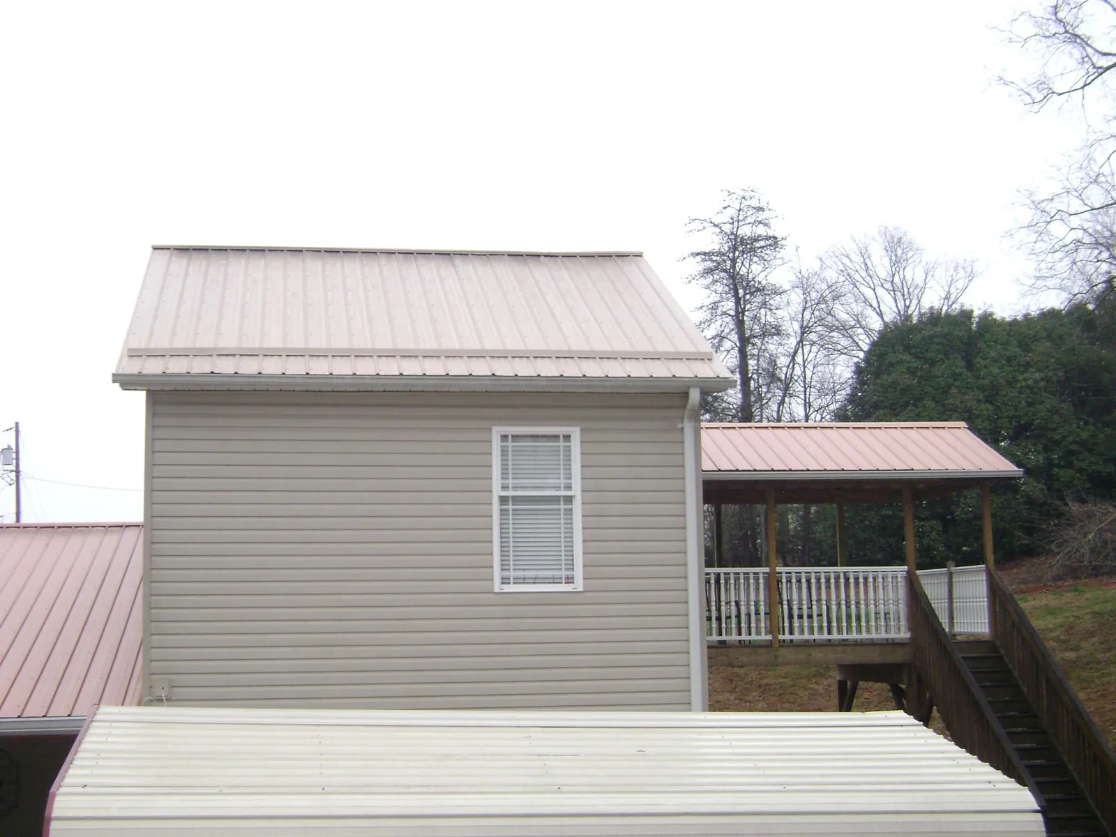 Tan metal roofs on a two story addition and attached porch, from a Roof Replacement job in Flat Rock